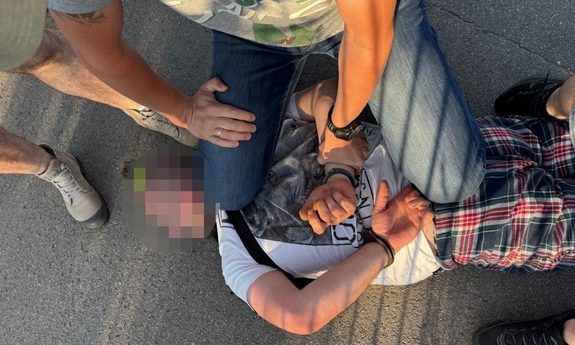 Policjant podczas zatrzymania mężczyzny, który leży na ziemi.