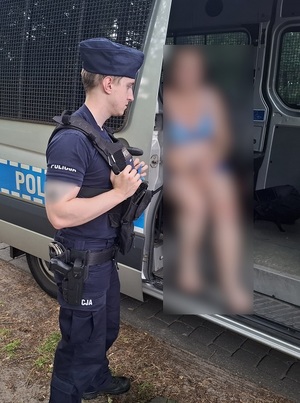 Kobieta w radiowozie. Obok stoi umundurowany policjant.