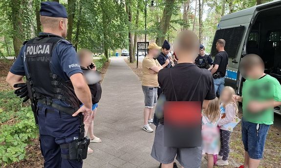 Policjanci przy radiowozie. Obok stoi kilka osób dorosłych i kilkoro dzieci.