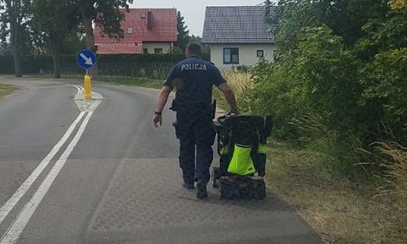 policjant prowadzi wózek inwalidzki.