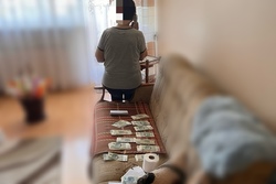 Zdjęcie przedstawia starszą osobę rozmawiającą przez telefon. Widoczne pieniądze przygotowane dla sprawcy oszustwa.