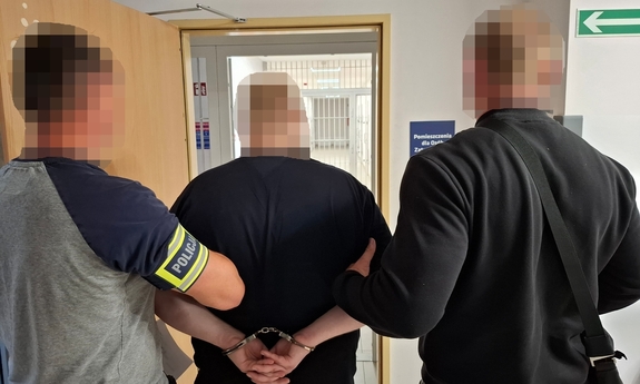 Dwaj policjanci prowadzą zatrzymanego mężczyznę.