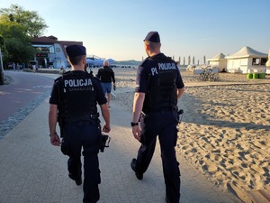 dwóch policjantów idzie wzdłuż plaży.