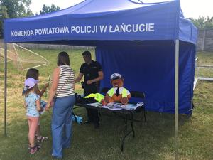 Policjant w namiocie profilaktycznym rozmawia z uczestnikami pikniku.