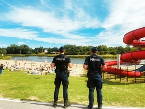 Dwaj policjanci odwróceni tyłem patrolują plażę.