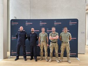 Trzej kontrterroryści i dwaj policjanci pozują do zdjęcia. W tle ścianka Ambasady RP w Berlinie.