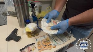 Policjant trzyma w rękach zabezpieczone pieniądze. Na blacie przy, którym stoi leżą pieniądze i pistolet.