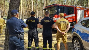 Policjant w towarzystwie trzech strażaków podczas wizytacji obozu harcerskiego.