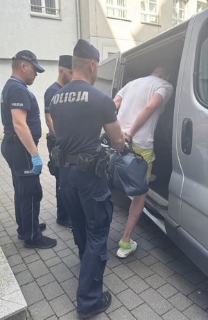 Policjanci prowadzą do radiowozu zatrzymanego.