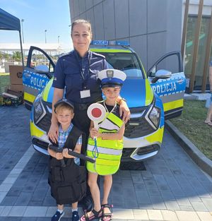 Policjantka pozuje do zdjęcia z dziećmi za nimi radiowóz.