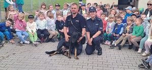 Para policjantów pozuje do zdjęcia z grupą dzieci, obok leży pies służbowy.