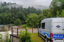 Zdjęcie przedstawia oznakowany radiowóz policyjny typu furgon w trakcie monitorowania przez policjantów poziomu rzeki.