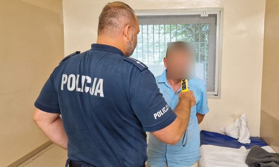 Policjant bada zatrzymanego mężczyznę alkomatem.