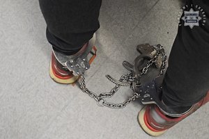 Na zdjęciu widoczne są nogi mężczyzny, na które ma założone kajdanki zespolone.