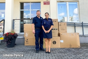 Policjantka i policjant, za nimi kartony z zebranymi darami.