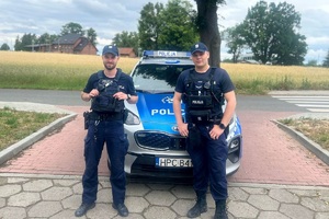Dwaj policjanci stoją przy radiowozie.
