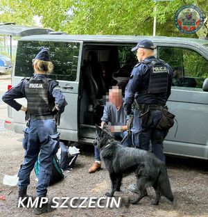 Dwoje policjantów z psem przy samochodzie, gdzie na podłodze siedzi mężczyzna.