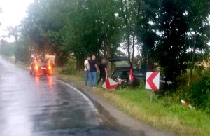 Trzej mężczyźni przy rozbitym aucie, które wypadło z drogi.