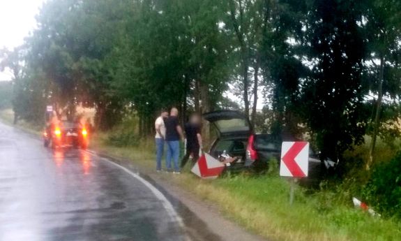 Trzej mężczyźni przy rozbitym aucie, które wypadło z drogi.