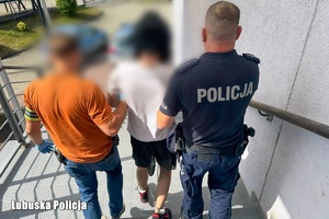 Dwaj policjanci, jeden ubrany po cywilnemu, drugi umundurowany, prowadzą zatrzymanego.