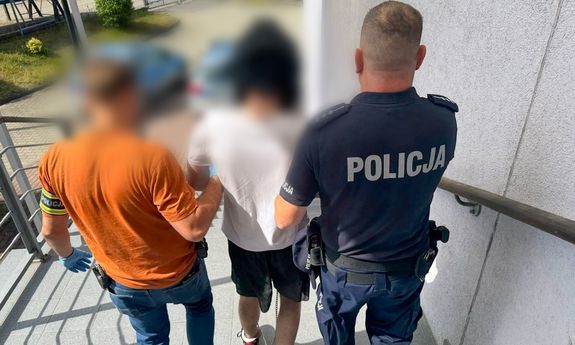 Dwaj policjanci, jeden ubrany po cywilnemu, drugi umundurowany, prowadzą zatrzymanego.