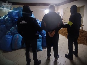 Dwaj funkcjonariusze trzymają zatrzymanego.