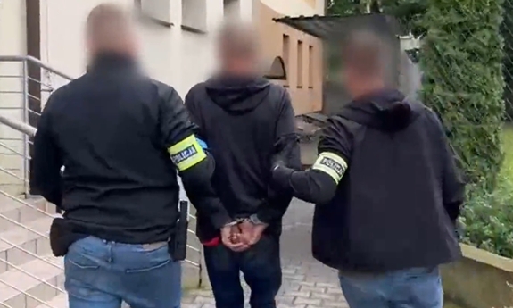 Zatrzymany mężczyzna prowadzony przez dwóch policjantów.