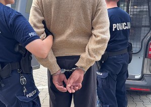 Dwaj policjanci prowadzą zatrzymanego w kajdankach.
