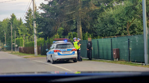 Dwaj policjanci stoją przy radiowozie z młodym chłopakiem.