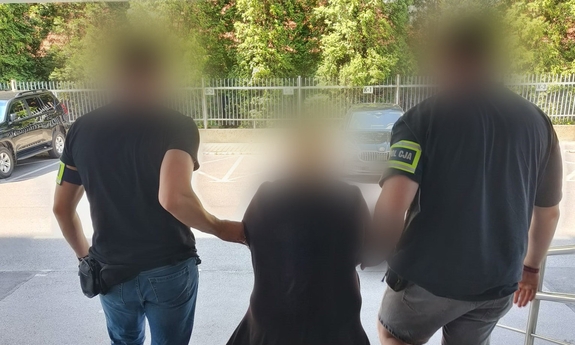 Dwaj nieumundurowani funkcjonariusze prowadza zatrzymaną kobietę.