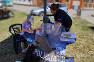 Policjantka z dziećmi przy stoisku profilaktycznym.