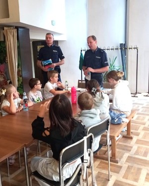 Dwaj policjanci prowadzą spotkanie profilaktyczne dla dzieci przebywających na półkoloniach.