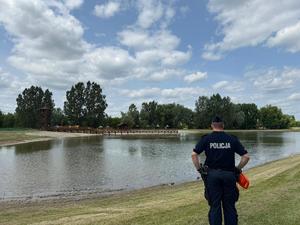 Policjant stoi nad brzegiem akwenu wodnego.