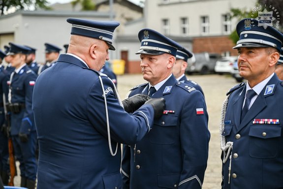Oficer Policji przypina policjantowi w mundurze odznaczenie.