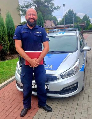 Sierż. szt. Wiesław Cudo w mundurze. W tle policyjny radiowóz.