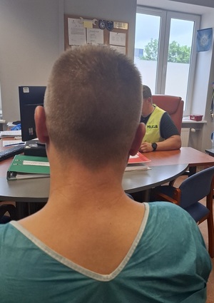 Zatrzymany mężczyzna siedzi tyłem. Z boku widać przesłuchującego go policjanta.