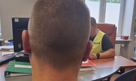 Zatrzymany mężczyzna siedzi tyłem. Z boku widać przesłuchującego go policjanta.