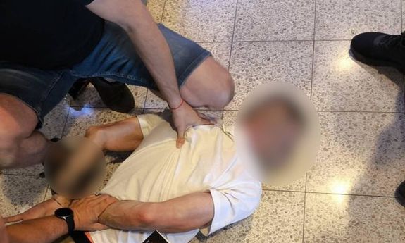 Policjanci przytrzymują leżącego na ziemi zatrzymanego, skutego w kajdanki.