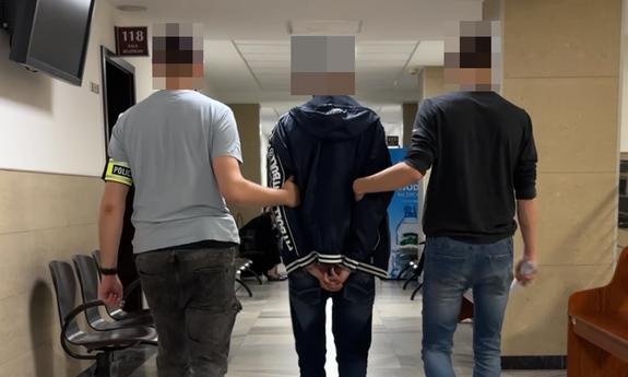 Dwaj funkcjonariusze prowadza zatrzymaną osobę korytarzem.