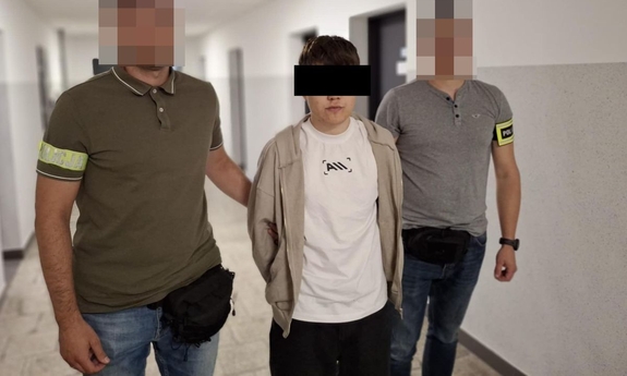 Dwaj policjanci prowadzą zatrzymanego mężczyznę korytarzem.