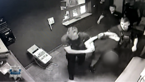 Stopklatka z nagrania monitoringu. Policjanci prowadza zatrzymanego mężczyznę.