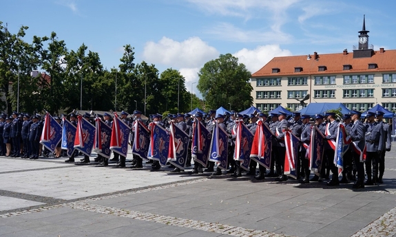 Policjanci stoją w szeregach na placu ze sztandarami podczas uroczystości.