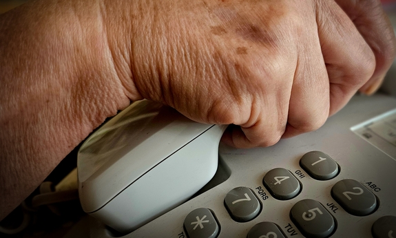 Dłoń na słuchawce telefonu stacjonarnego.