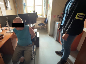 Zatrzymany mężczyzna siedzi na krześle, a obok niego stoi nieumundurowany policjant.