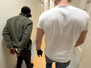 Nieumundurowany policjant prowadzi zatrzymanego korytarzem.