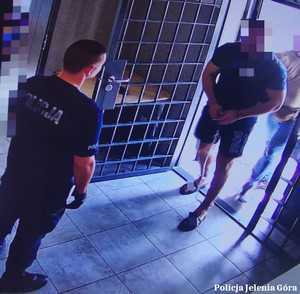 Policjant z zatrzymanym, skutym w kajdanki mężczyzną.