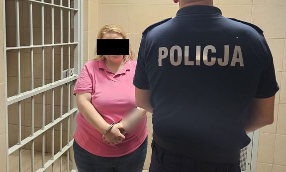 Zatrzymana kobieta i stojący tyłem policjant, u którego widać napis na plecach: Policja.