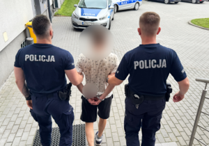 Dwaj policjanci prowadzą zatrzymanego mężczyznę.