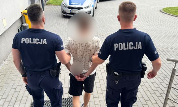 Dwaj policjanci prowadzą zatrzymanego mężczyznę.