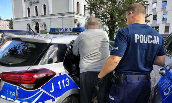 Policjant prowadzi zatrzymanego do radiowozu.